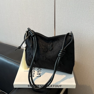 Black tote bag with butterfly embroidery and tassel charm on a book background