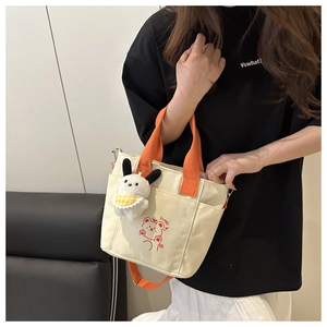 Detail of canvas tote bag with orange strap, cartoon bear print, and plush bunny charm