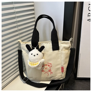 Detailed view of cream canvas tote bag featuring a red cartoon bear and plush charm