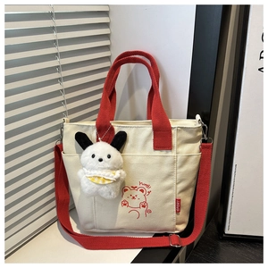 Detail of white canvas tote with red handles featuring a cartoon bear print and plush dog charm