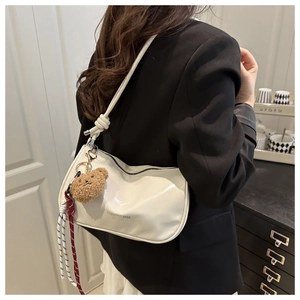 Model wearing a white glossy crescent shoulder bag with a cute plush bear charm detail