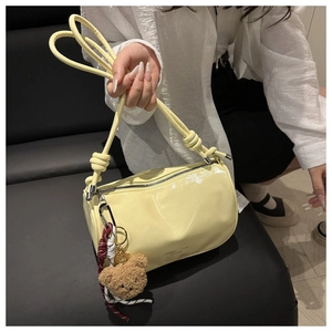 Detail of light yellow cylinder handbag with a glossy finish and brown plush bear charm