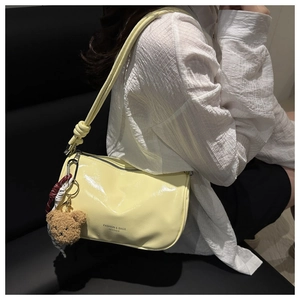 Detailed shot of yellow patent leather crescent bag with bear charm and zipper closure