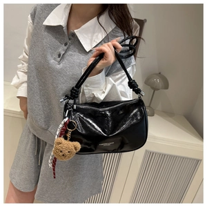 Detail of black patent leather shoulder bag featuring a teddy bear charm and ribbon