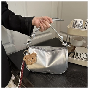 Detail of silver metallic crescent bag with knotted strap and cute plush bear charm