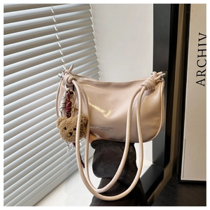 Detail of light pink shoulder bag with glossy finish and brown plush bear charm accessory