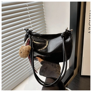 Detail of black glossy shoulder bag with a brown plush bear charm and knotted strap decor