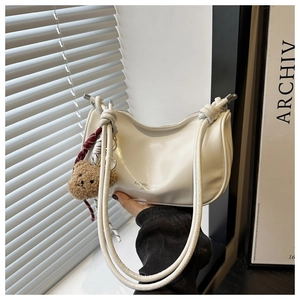 Detail of white PU leather crescent shoulder bag with a cute plush bear pendant accessory