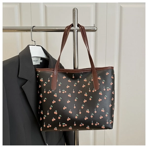 Gros plan du sac cabas en cuir noir avec imprimé cerises et fines bandoulières brunes