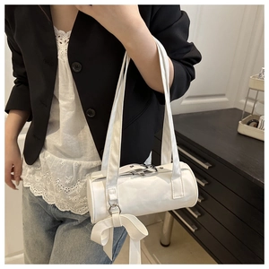 Detailed view of white cylindrical baguette bag featuring a large decorative side bow