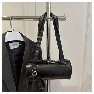 Close-up of black leather cylinder Boston bag with a large bow charm on a metal hanger