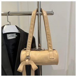 Detail of cream cylindrical shoulder bag with elegant bow accent and silver metal hardware