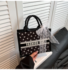 Detail of black tote bag with white bow pattern and elegant lace bow charm accessory