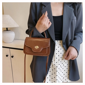 Close-up of a brown leather crossbody bag with a gold metal twist lock and top handle