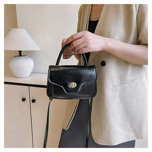 Detailed close-up of a black vintage handbag featuring a gold metal twist-lock and glossy leather
