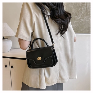 Modern black crossbody bag with gold lock buckle shown on model in minimal interior