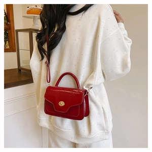 Detail of red patent leather handbag featuring a golden circular twist-lock closure