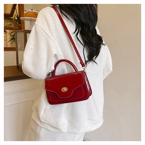 Detail view of a bright red patent leather handbag with gold clasp and chain strap