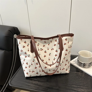 Retro white tote bag with red cherry print and brown handles on dark wood table