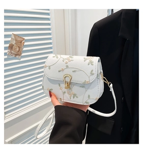 Détail de la broderie florale sur un sac blanc avec fermoir en fer à cheval doré