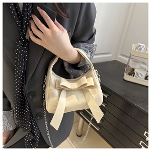 Détail d'un sac à main beige avec nœud papillon et chaîne argentée au look chic