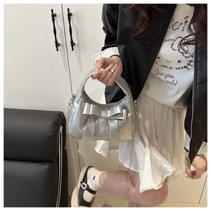 Détail du sac argenté métallisé avec un grand nœud et une bandoulière sur un mannequin