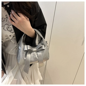 Détail du sac argenté avec nœud papillon, bandoulière chaîne et fermeture à glissière