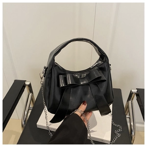 Détail du sac à main en cuir verni noir avec grand nœud et bandoulière chaîne