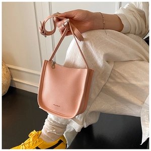 Detail of pink pebbled leather bucket bag with brand logo and slim shoulder strap