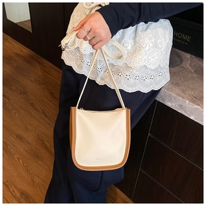 Detailed view of cream bucket bag showing lychee grain leather and brown trim edges