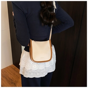 Detail of a minimalist cream bucket bag with brown trim worn by a model in a casual setting
