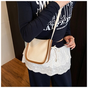 Detail of off-white lychee grain leather crossbody bag with brown contrast trim and slim strap