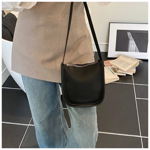 Detail of a black pebbled leather bucket bag with slim shoulder strap worn on the body