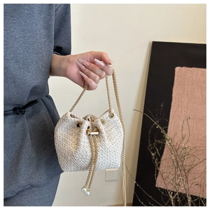 Close-up of woven bucket bag featuring pearl drawstring tassels and a gold chain strap