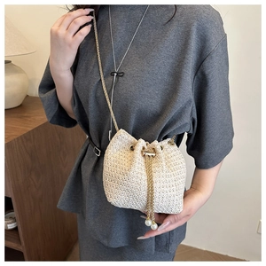 Detail of straw bucket bag featuring pearl drawstring accents and gold chain strap