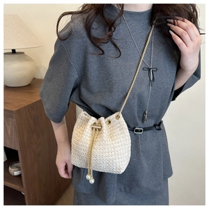 Detail of woven straw bucket bag with gold chain strap and elegant pearl drawstring charms