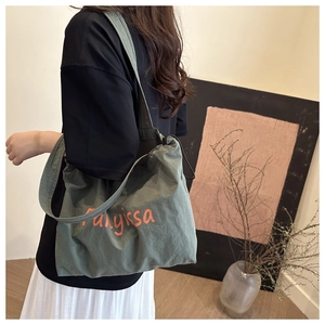 Détail du sac fourre-tout en toile vert foncé avec imprimé de lettres orange et bandoulière large