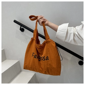 Detail view of burnt orange nylon tote bag featuring drawstring closure and black lettering