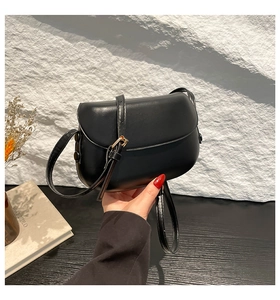 Detail of a black leather saddle bag featuring a smooth finish and adjustable shoulder strap