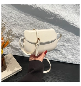 Detail of off-white faux leather saddle bag on a minimalist stone and black surface