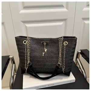 Detail of black woven tote bag with golden deer pendant and chain strap on a book