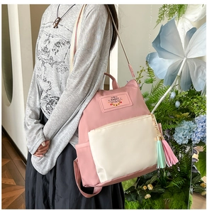 Détail du sac à dos en nylon rose et beige avec pompons et étiquette tissée
