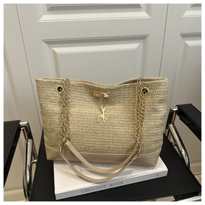 Detail of woven straw tote bag with golden deer charm and chain strap accents