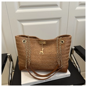 Detail of V-shaped woven straw tote bag with gold chain and metal deer pendant