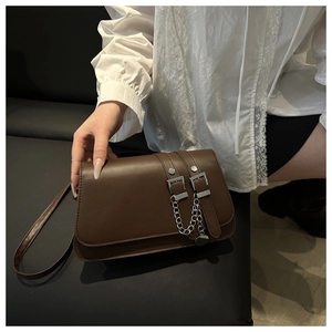 Detail of dark brown baguette bag with double belt buckles and silver metal chains