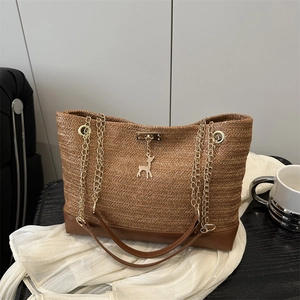 Sac fourre-tout en paille avec base en cuir marron et pendentif cerf doré sur fond blanc