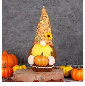 Detail of plush gnome holding small pumpkin with sunflower pattern hat for fall decor