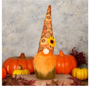 Close-up of harvest gnome with sunflower patterned hat among pumpkins and autumn leaves