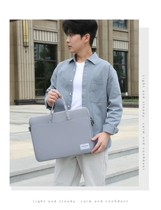 Grey minimalist laptop sleeve bag with handle carried by a model in business casual attire