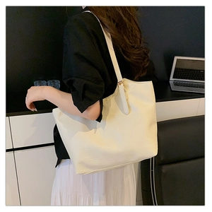 Detailed side view of the spacious cream tote bag worn by a model in an office setting